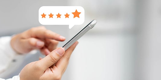 Close-up of hands holding a smartphone with a five-star rating pop-up icon appearing above the device.