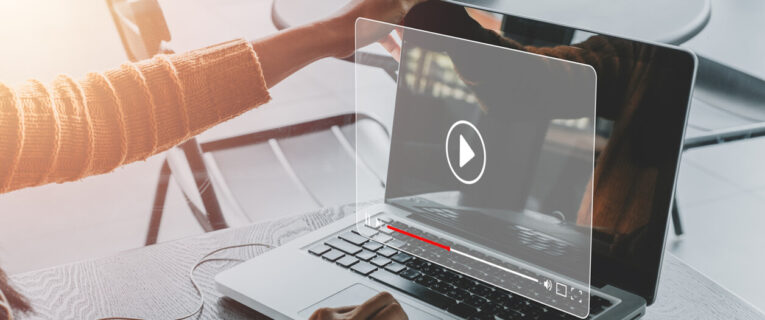 A person wearing an orange sleeve interacts with a transparent screen overlay on a laptop displaying a play button for a video.