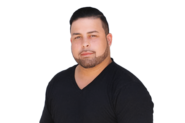 A man with short dark hair and a beard, wearing a black V-neck shirt, looks directly at the camera against a white background.