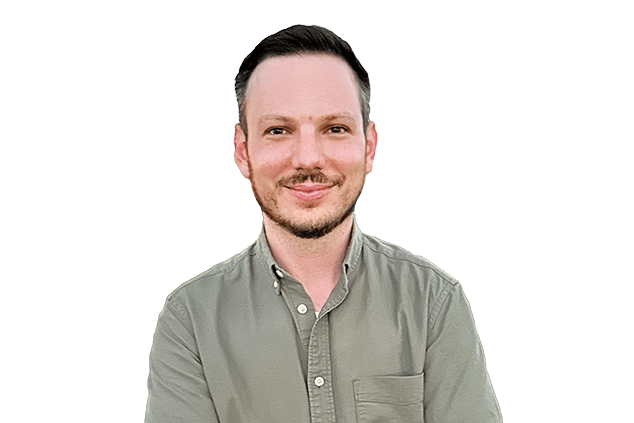 A man with short dark hair and a trimmed beard, wearing a button-up olive green shirt, stands against a plain white background.